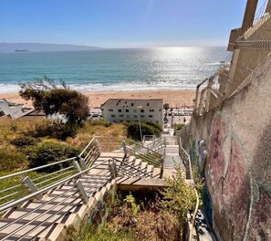 A staircase leading to a beach with a view of the ocean and a building in the background. - Urbano Familiar Bellavista Parking Washer Wifi (Vina del Mar)