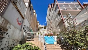 Un estrecho callejón urbano con grafitis, una escalera y un edificio con una escalera metálica a la derecha.
