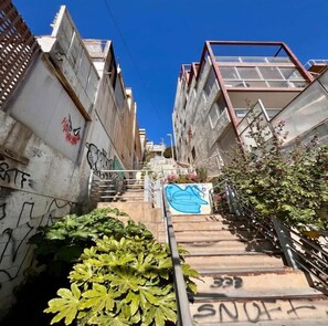 Um beco urbano estreito com grafite, uma escadaria e um edifício com escada metálica à direita.