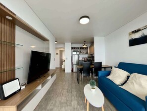A modern living room with a blue sofa, a flat-screen TV, and a small white table with a plant. - Urbano Familiar Bellavista Parking Washer Wifi (Vina del Mar)
