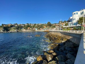 A coastal view with a rocky shoreline, clear blue water, and a bridge leading to a hillside with buildings. - Caba a Estudio BBQ Kitchen Parking Pet Wifi (Casablanca)