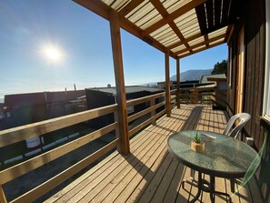 A wooden deck with a glass balustrade overlooking a body of water, a round table with a plant, and a clear sky. - Caba a Estudio BBQ Kitchen Parking Pet Wifi (Casablanca)