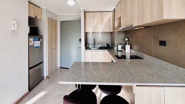 A modern kitchen with a granite countertop, stainless steel appliances, and wooden cabinets. - Urbano Plaza Vespucio Laundry Parking Pet Pool (Santiago)
