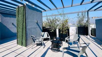 A rooftop terrace with a modern design, featuring a seating area with chairs and tables, a decorative wall with greenery, and potted plants.