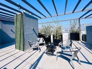 Une terrasse sur le toit au design moderne, comprenant un espace salon avec des chaises et des tables, un mur décoratif agrémenté de plantes grimpantes et des plantes en pot.