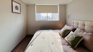 A bedroom with a bed, a window, and a city view. - Urbano Plaza Vespucio Laundry Parking Pet Pool (Santiago)