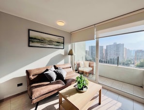 Un salon moderne avec un canapé marron, une table basse en bois agrémentée d’une plante, et une vue sur la ville à travers de grandes fenêtres.