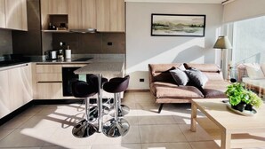 A modern kitchen with a dining area, a sofa, and a coffee table. - Urbano Plaza Vespucio Laundry Parking Pet Pool (Santiago)