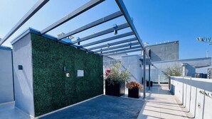 A rooftop terrace with a green wall, potted plants, and a clear blue sky. - Urbano Plaza Vespucio Laundry Parking Pet Pool (Santiago)
