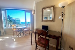 Et værelse med balkon, skrivebord med computer, stol og lampe.
