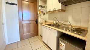 Una cocina compacta con puerta de madera, armarios blancos, un lavamanos de acero inoxidable y una estufa integrada.