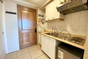 A compact kitchen with a wooden door, white cabinets, a stainless steel sink, and a built-in stove. - Estudio Playa Miramar Home Office Pool Parking (Vina del Mar)
