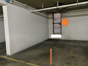 En parkeringskælder med betonvægge, en metalventil i loftet og et afløb på gulvet.