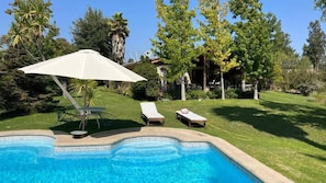 Ein Pool mit Liegestühlen und Sonnenschirm, umgeben von einem gepflegten Rasen und Bäumen.