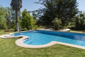 A swimming pool with a curved edge, surrounded by well-maintained grass and trees. - Casa Foresta BBQ Parking Pet Swimming Pool Wifi (Melipilla)
