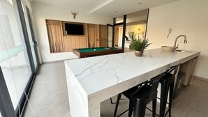 A modern kitchen with a marble countertop, a pool table, and a potted plant. - Estudio Dubl Almeyda Crib Laundry Gym Pool (Santiago)