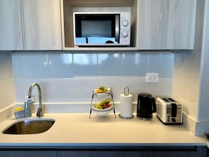 A kitchen with a stainless steel sink, a microwave, a fruit bowl, a coffee maker, and a toaster. - Estudio Dubl Almeyda Crib Laundry Gym Pool (Santiago)