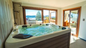 A hot tub in a room with large windows, a view of a lake, and a balcony with outdoor furniture. - Casa Playa Hermosa BBQ Jacuzzi Parking Wifi (Puerto Varas)