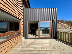 Een modern gebouw met een houten terras, grote schuifpuien en uitzicht op het landschap.
