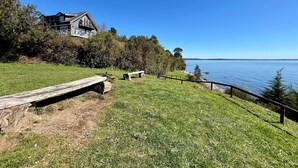 A grassy area with a wooden bench and a fence overlooking a body of water. - Casa Playa Hermosa BBQ Jacuzzi Parking Wifi (Puerto Varas)