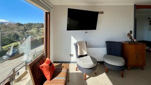 A modern living room with a large window, a flat-screen TV, a sofa, two armchairs, and a wooden cabinet. - Casa Playa Hermosa BBQ Jacuzzi Parking Wifi (Puerto Varas)