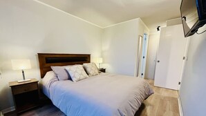 A bedroom with a bed, nightstands, a TV, and a door. - Urbano Familiar Bustamante Laundry Parking Pool (Santiago)