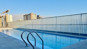 A swimming pool with metal railings, a tiled deck, and a view of buildings in the background. - Urbano Familiar Bustamante Laundry Parking Pool (Santiago)