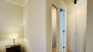 A hallway with a wooden floor, a desk with a lamp, and a wardrobe with two doors. - Urbano Familiar Bustamante Laundry Parking Pool (Santiago)