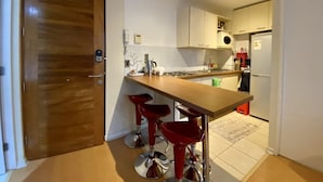 Una cocina compacta con encimera de madera, dos taburetes rojos, un refrigerador y un microondas.