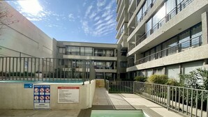Zona de piscina con un cartel que detalla las normas de la piscina, rodeada por un edificio de varios pisos con balcones.