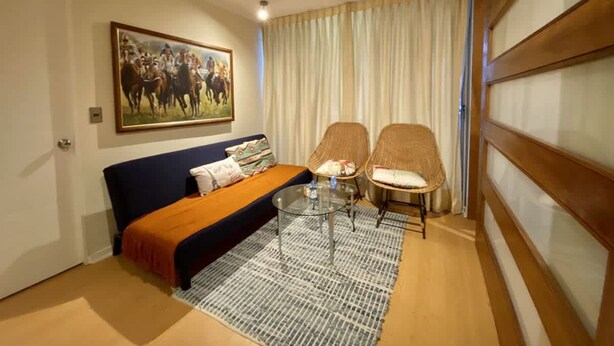 Una habitación con sofá, dos sillones, una mesita de centro, un cuadro y una ventana con cortinas.