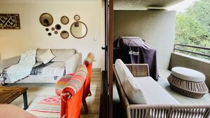 A living room with a sofa, a coffee table, and a patterned rug. There are wall decorations and a grill outside. - Buho Modern Nature Retreat - Puc n (Pucón)