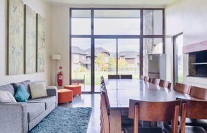 A spacious living room with a large dining table, a sofa, and a view of a residential area through large windows. - Buho Modern Nature Retreat - Puc n (Pucón)