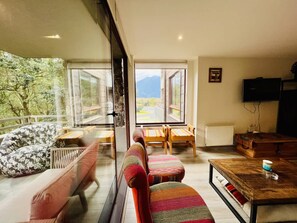 A cozy living room with a sofa, a coffee table, and a view of a mountain landscape through large windows. - Buho Modern Nature Retreat - Puc n (Pucón)