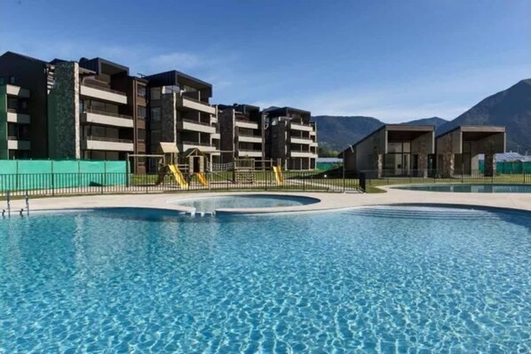 A swimming pool surrounded by modern buildings with balconies, set against a mountainous backdrop. - Buho Modern Nature Retreat - Puc n (Pucón)