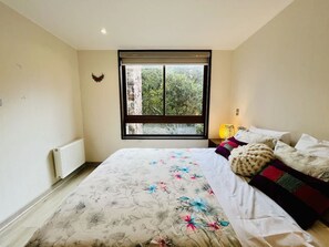 A bedroom with a large bed, a window with a view of trees, a radiator, and a wall-mounted light. - Buho Modern Nature Retreat - Puc n (Pucón)