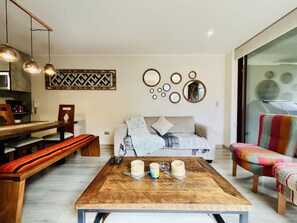 A modern living room with a wooden coffee table, a sofa, a colorful armchair, and a dining area with a bench and table. - Buho Modern Nature Retreat - Puc n (Pucón)