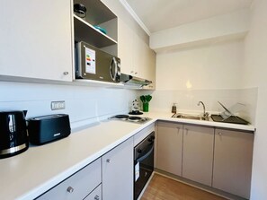 Una cucina compatta con forno integrato, macchina del caffè, lavello e microonde.