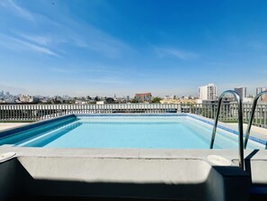 Piscina en la azotea con vistas a la ciudad, barandillas metálicas y cielo despejado.