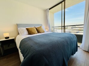 Una habitación de hotel con una cama, una mesita de noche, una ventana con vistas y un balcón.