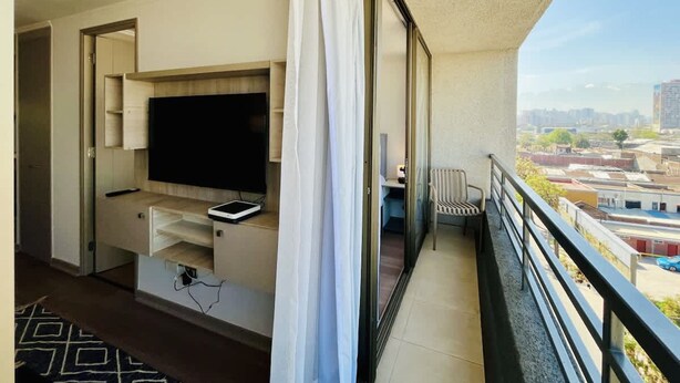 A balcony with a TV, a chair, and a view of the cityscape. - Urbano Esperanza Plaza Yungay Laundry Pet Pool (Santiago)