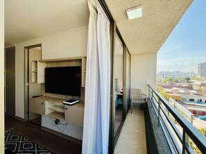 Un balcón con televisión, una silla y vista a la ciudad.