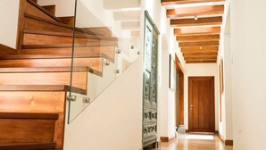 Eine Holzt Treppe mit Glastrelings, die zu einem Flur mit Holzbalken an der Decke führt.
