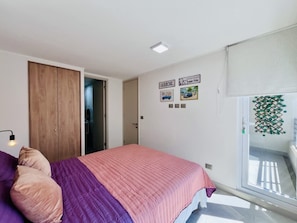 Ein Schlafzimmer mit Bett, Kleiderschrank, Tür, Bildern an der Wand und einem Fenster.