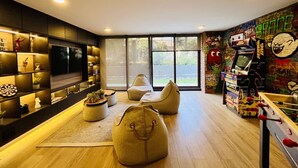 Una sala de estar moderna con un televisor de pantalla plana, asientos cómodos y una zona de juegos con máquinas de arcade.