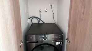 Un lavadero pequeño con una lavadora Midea y un armario negro encima.