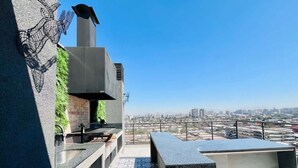 Una terraza en la azotea con cocina moderna, asientos exteriores y vistas a la ciudad.