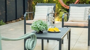 Eine Terrasse mit zwei Stühlen, einem Tisch, einer kleinen Pflanze und einer Obstschale.