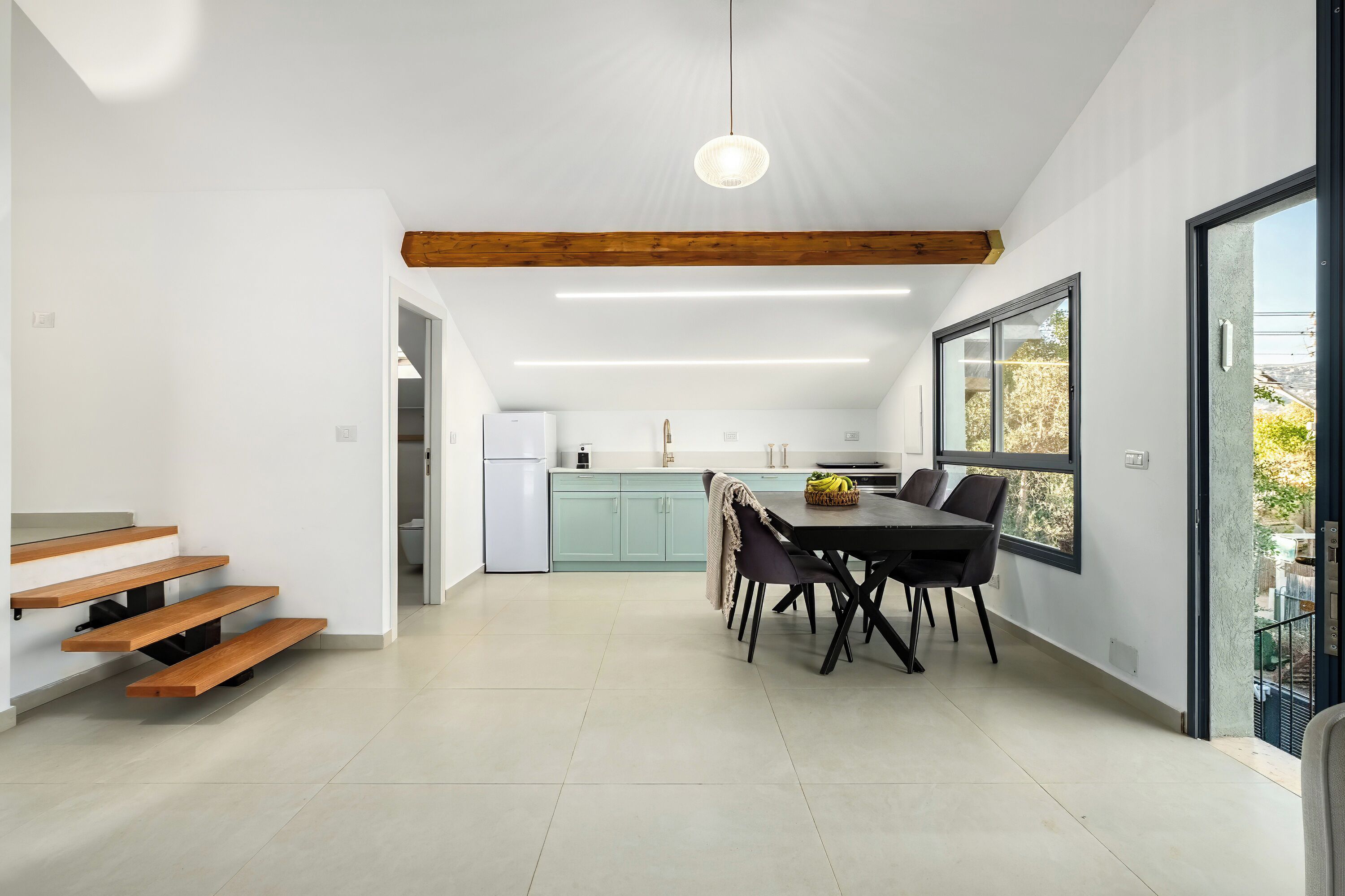 A modern kitchen with a dining area, wooden beams, and a large window.