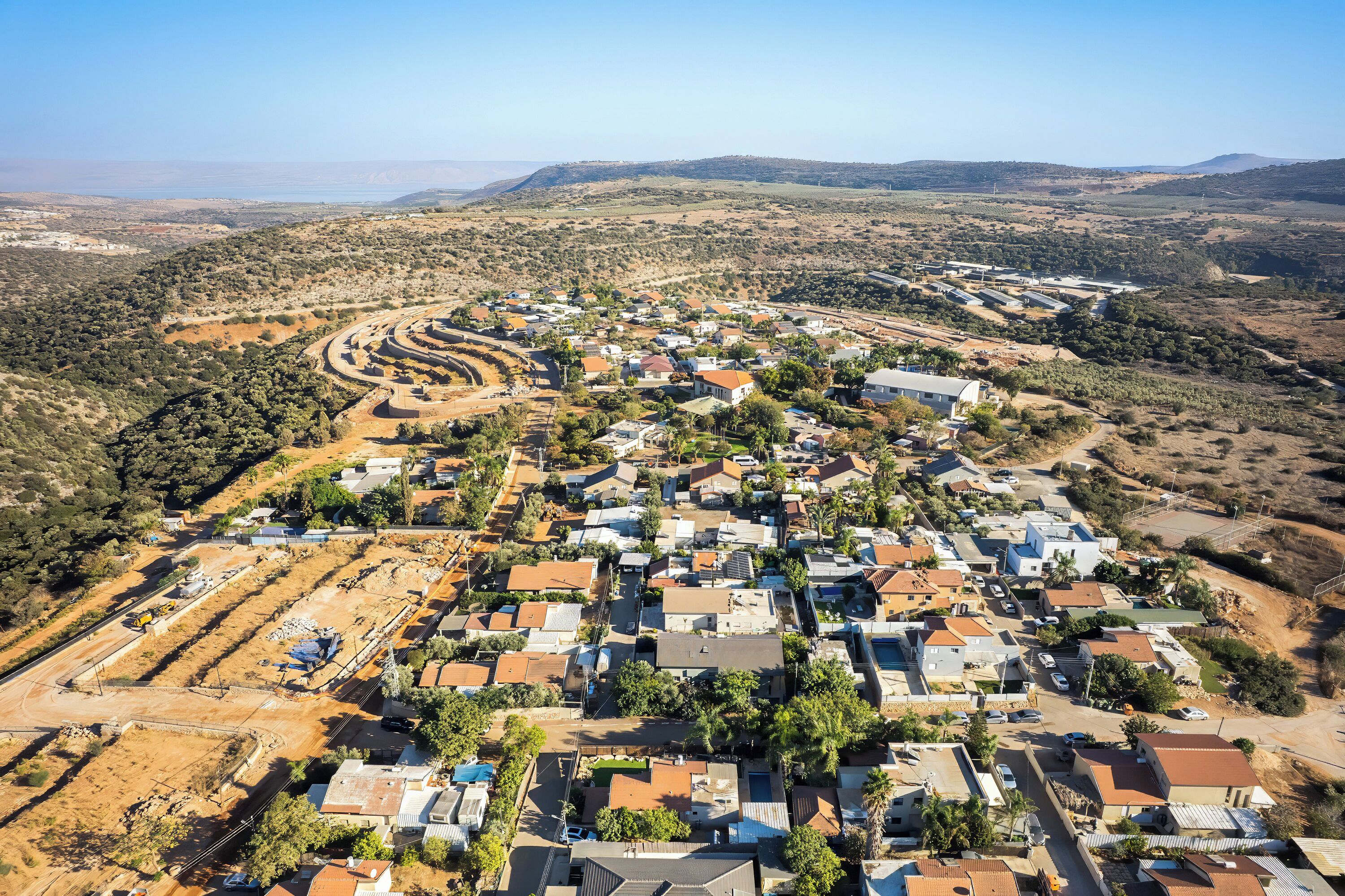 An aerial view of a residential area with houses, roads, and a hilly landscape in the background.